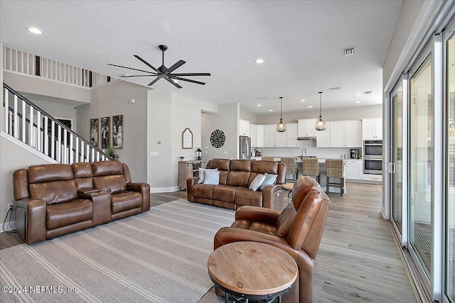 living room with a textured ceiling, light wood-type flooring, ceiling fan, and sink