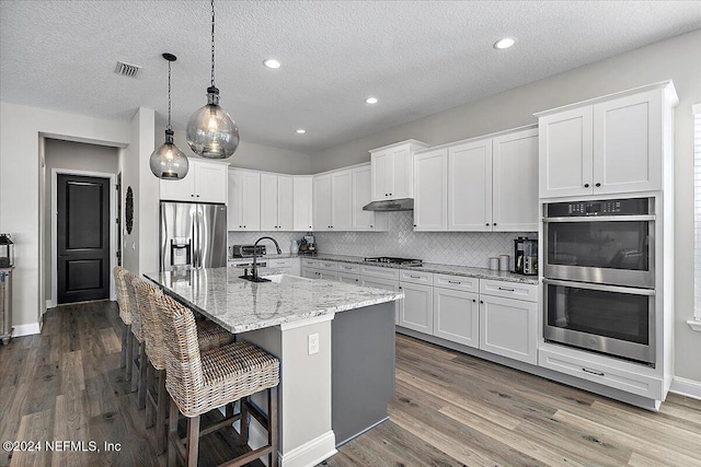 kitchen featuring white cabinetry, an island with sink, stainless steel appliances, and a textured ceiling