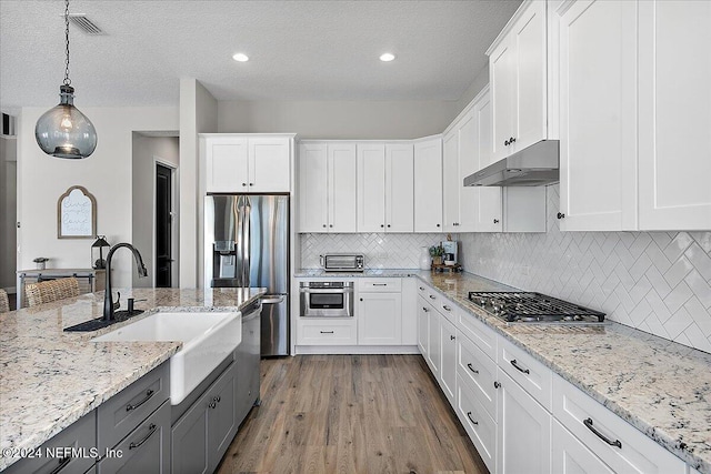 kitchen featuring appliances with stainless steel finishes, a textured ceiling, pendant lighting, hardwood / wood-style flooring, and white cabinets