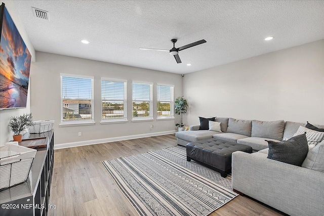 living room with a textured ceiling, light wood-type flooring, and ceiling fan