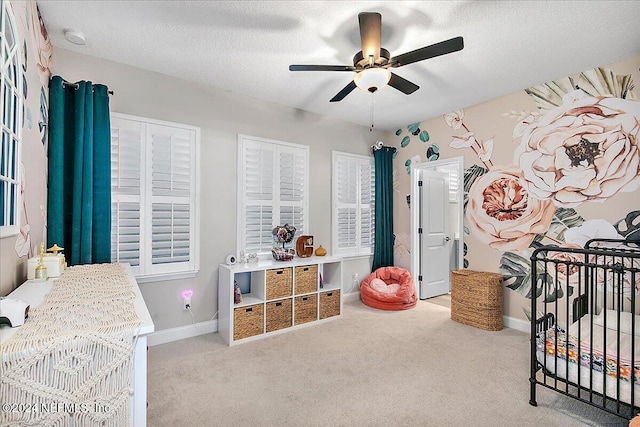 bedroom featuring light carpet, a textured ceiling, a nursery area, and ceiling fan