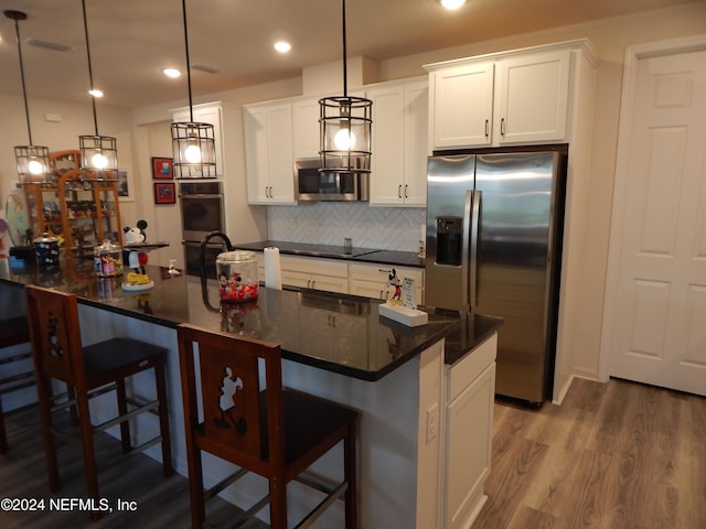 kitchen with stainless steel appliances, decorative light fixtures, hardwood / wood-style floors, white cabinetry, and an island with sink