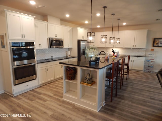 kitchen featuring a breakfast bar, light hardwood / wood-style flooring, an island with sink, appliances with stainless steel finishes, and decorative light fixtures