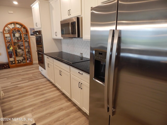 kitchen featuring dark stone countertops, appliances with stainless steel finishes, decorative backsplash, white cabinets, and light wood-type flooring