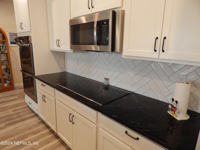 kitchen with decorative backsplash, appliances with stainless steel finishes, dark stone countertops, white cabinets, and light hardwood / wood-style floors