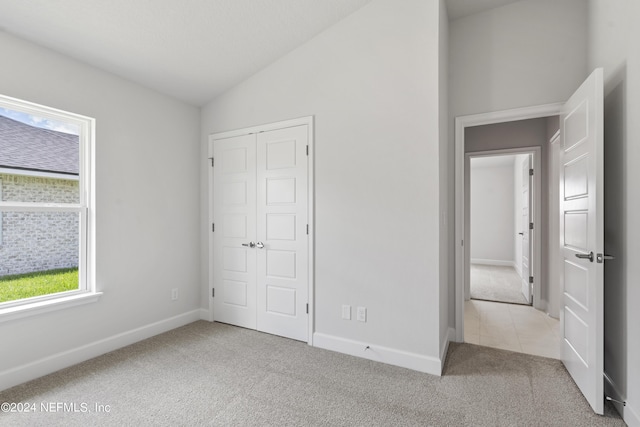 unfurnished bedroom with lofted ceiling, light carpet, and a closet