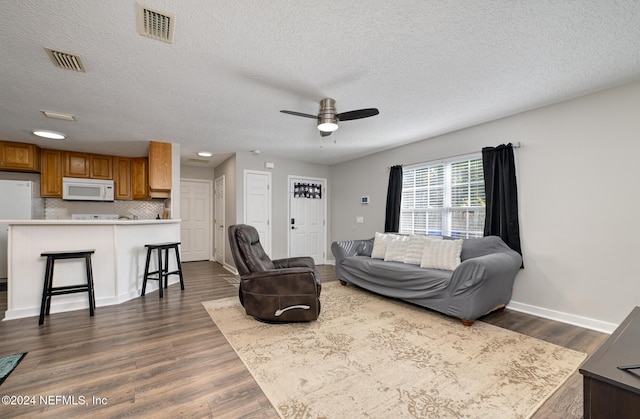 living room featuring ceiling fan, a textured ceiling, and dark wood-type flooring