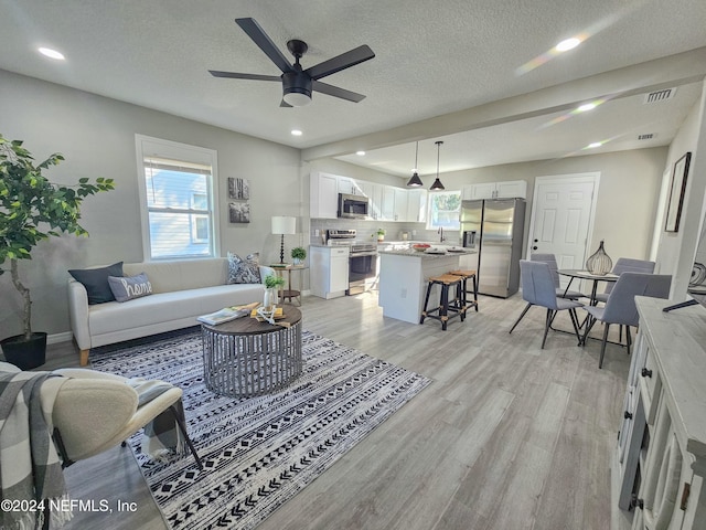 living room with a textured ceiling, light hardwood / wood-style flooring, and ceiling fan