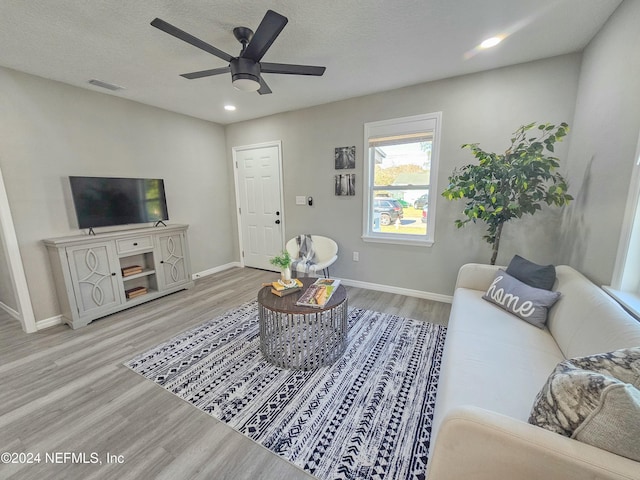 living room with a textured ceiling, light hardwood / wood-style flooring, and ceiling fan