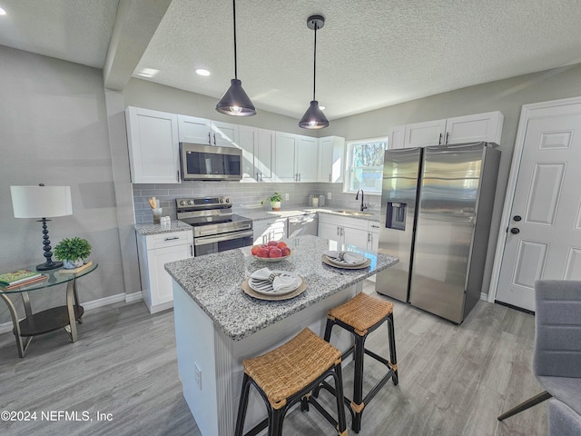 kitchen with white cabinets, a breakfast bar, appliances with stainless steel finishes, and light hardwood / wood-style flooring