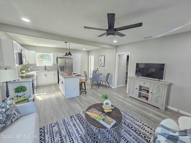 living room featuring ceiling fan, light hardwood / wood-style floors, and a textured ceiling