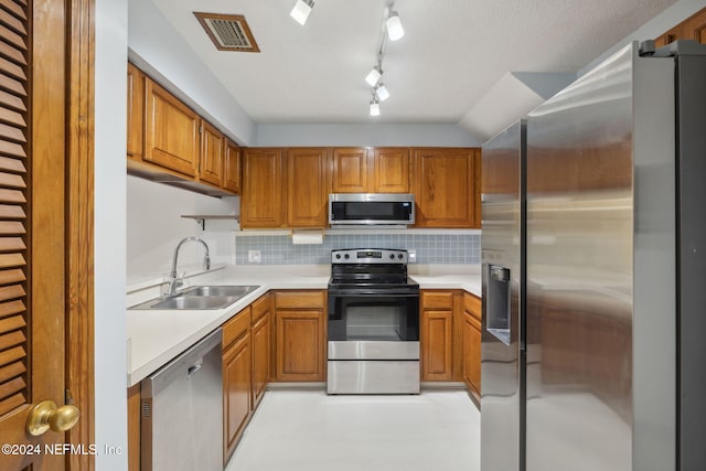 kitchen with lofted ceiling, rail lighting, sink, appliances with stainless steel finishes, and tasteful backsplash