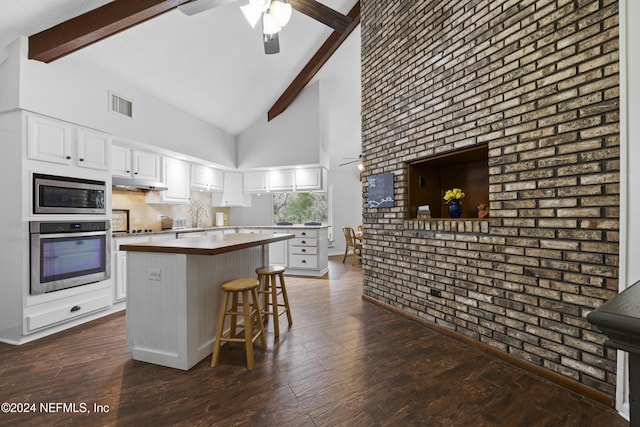 kitchen featuring stainless steel appliances, beamed ceiling, brick wall, a kitchen bar, and white cabinets