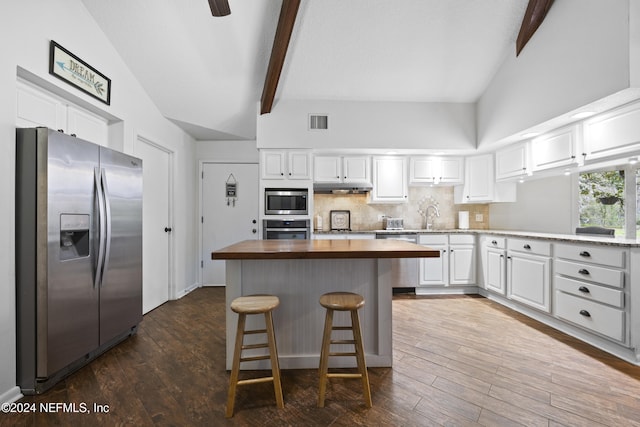 kitchen with beamed ceiling, wooden counters, backsplash, white cabinets, and appliances with stainless steel finishes