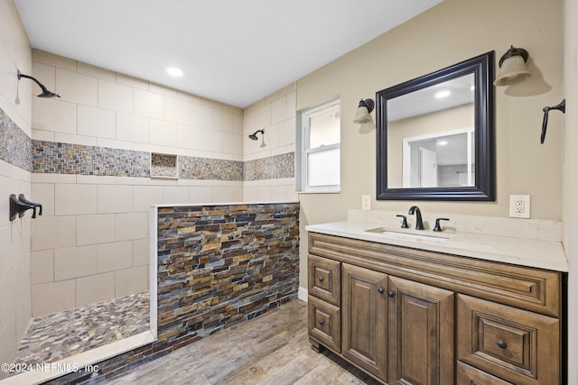 bathroom with hardwood / wood-style floors, vanity, and a tile shower