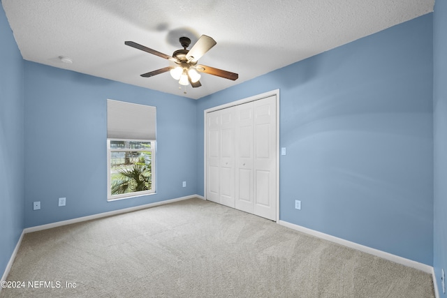 unfurnished bedroom with light carpet, a textured ceiling, a closet, and ceiling fan