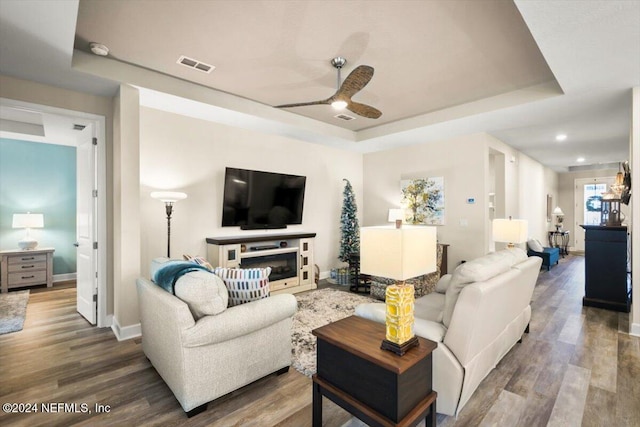 living room featuring a raised ceiling, ceiling fan, and wood-type flooring