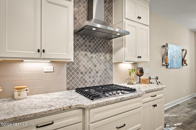 kitchen with decorative backsplash, light stone countertops, wall chimney exhaust hood, dark wood-type flooring, and stainless steel gas stovetop