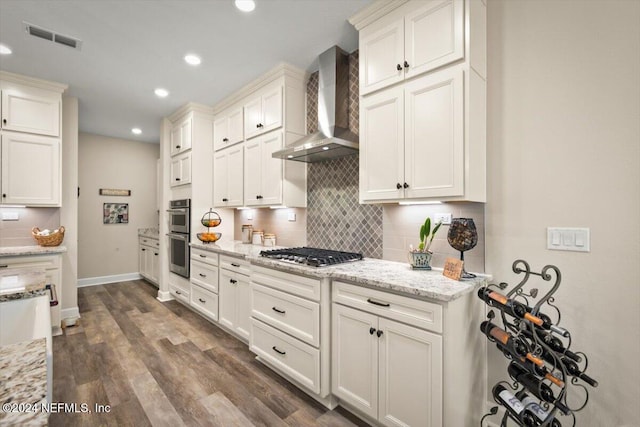 kitchen featuring light stone counters, wall chimney exhaust hood, stainless steel appliances, dark hardwood / wood-style floors, and white cabinetry