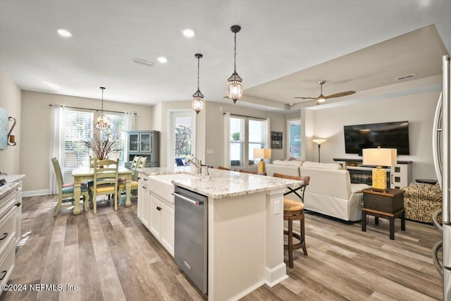 kitchen featuring dishwasher, a kitchen island with sink, sink, hanging light fixtures, and white cabinetry