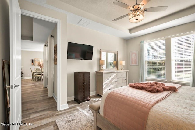 bedroom with ceiling fan, light hardwood / wood-style floors, and a raised ceiling