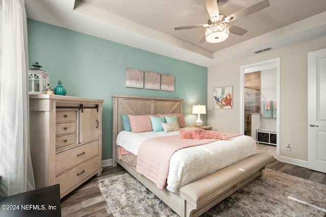 bedroom featuring ceiling fan, dark wood-type flooring, and a tray ceiling