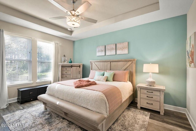 bedroom featuring ceiling fan, dark hardwood / wood-style flooring, and a tray ceiling