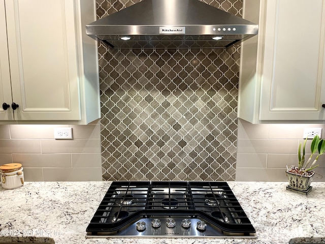 kitchen with decorative backsplash, gas cooktop, light stone counters, and wall chimney range hood