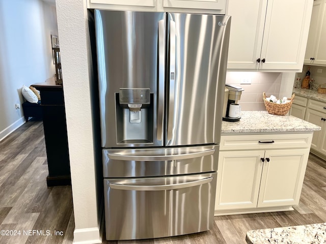 kitchen with decorative backsplash, stainless steel fridge, light stone counters, and hardwood / wood-style flooring