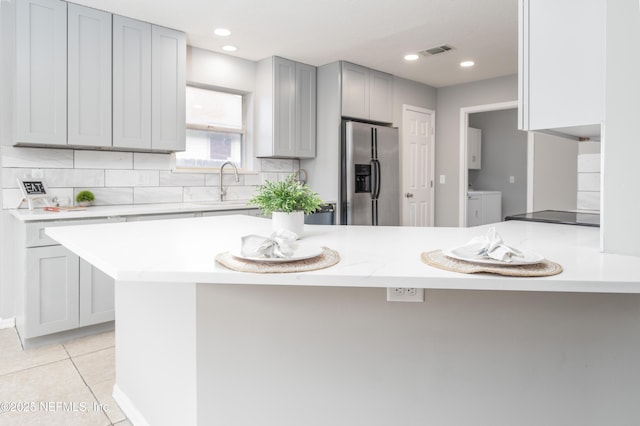 kitchen featuring sink, kitchen peninsula, washing machine and dryer, light tile patterned flooring, and stainless steel fridge with ice dispenser