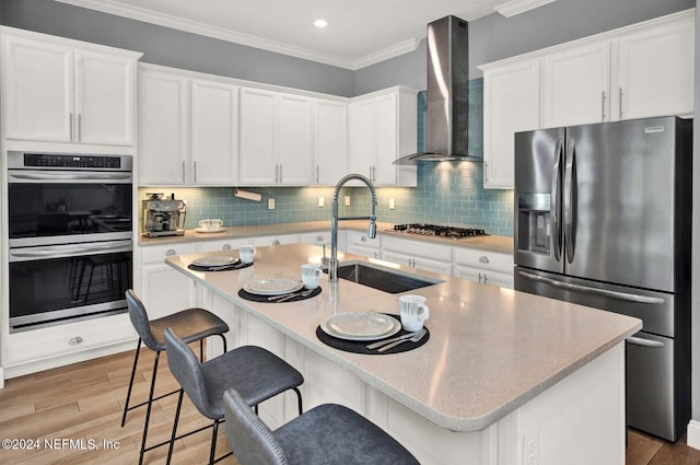 kitchen featuring light wood-type flooring, stainless steel appliances, white cabinetry, and wall chimney exhaust hood