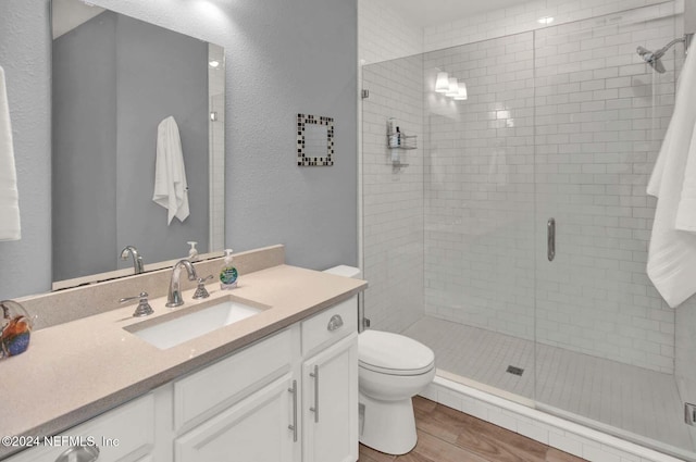 bathroom featuring a shower with door, vanity, wood-type flooring, and toilet