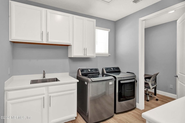 laundry area featuring separate washer and dryer, sink, cabinets, and light wood-type flooring