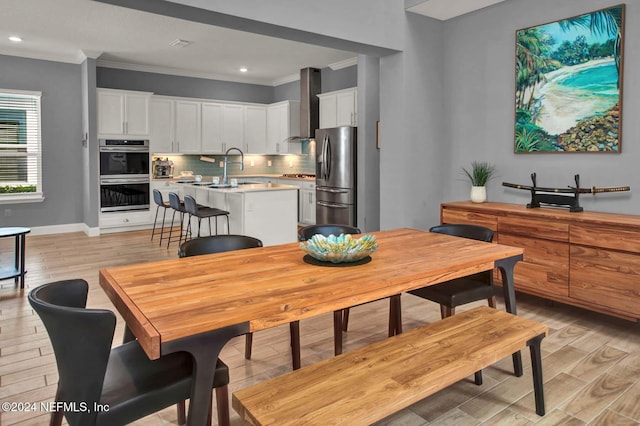 dining space with sink, ornamental molding, and light wood-type flooring