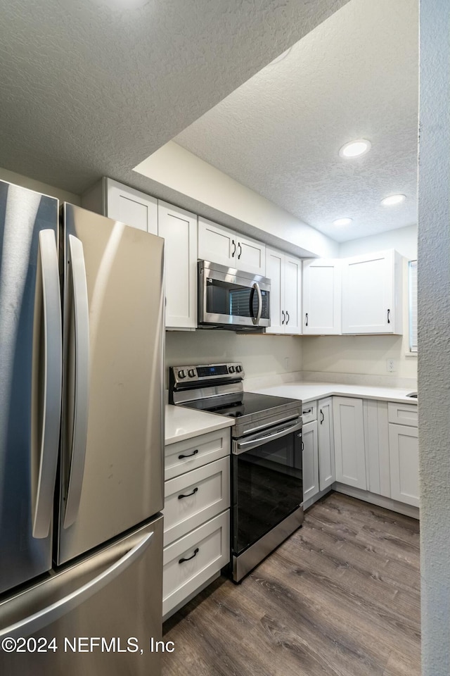 kitchen with dark wood-type flooring, white cabinets, stainless steel appliances, and a textured ceiling