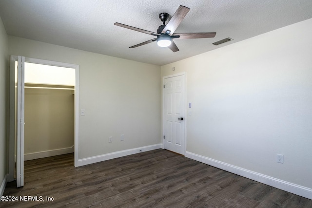 unfurnished bedroom featuring ceiling fan, dark hardwood / wood-style floors, a textured ceiling, a walk in closet, and a closet