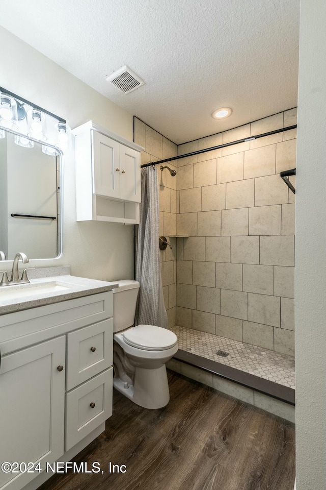 bathroom featuring vanity, hardwood / wood-style flooring, a shower with shower curtain, toilet, and a textured ceiling