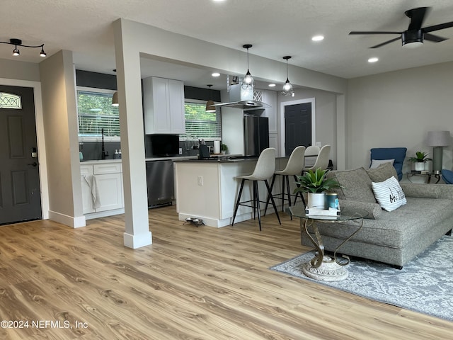 living room with ceiling fan, sink, light hardwood / wood-style floors, and a textured ceiling