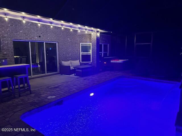 pool at night featuring a patio area