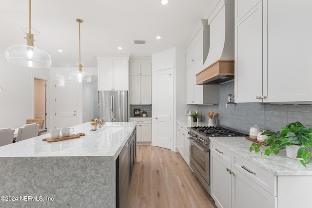 kitchen with stainless steel appliances, light hardwood / wood-style floors, decorative light fixtures, white cabinets, and custom range hood