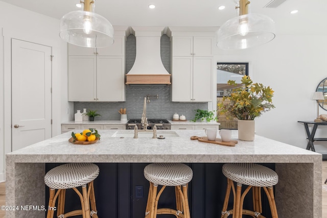 kitchen featuring white cabinetry, hanging light fixtures, a kitchen breakfast bar, an island with sink, and custom exhaust hood