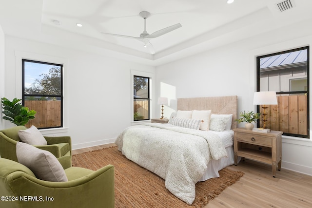 bedroom featuring a raised ceiling, ceiling fan, and light hardwood / wood-style flooring