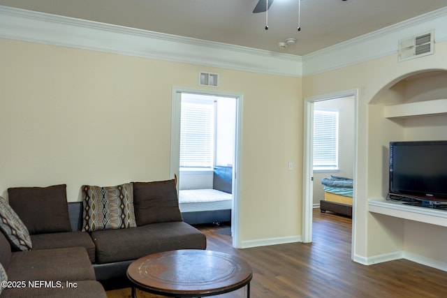 living room with dark hardwood / wood-style floors, built in features, a wealth of natural light, and ornamental molding