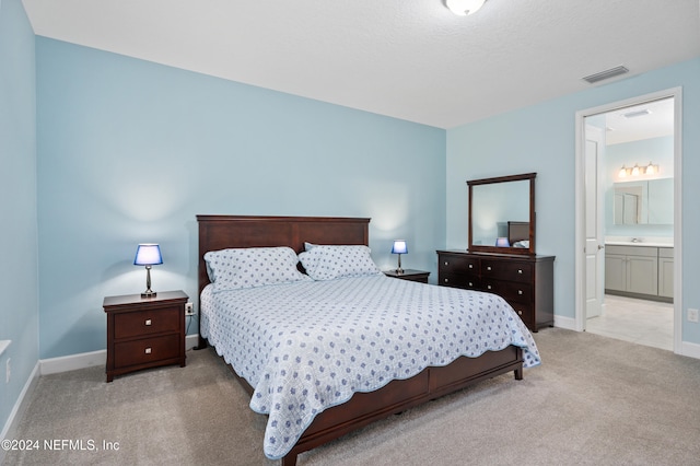 bedroom with connected bathroom, sink, and light colored carpet