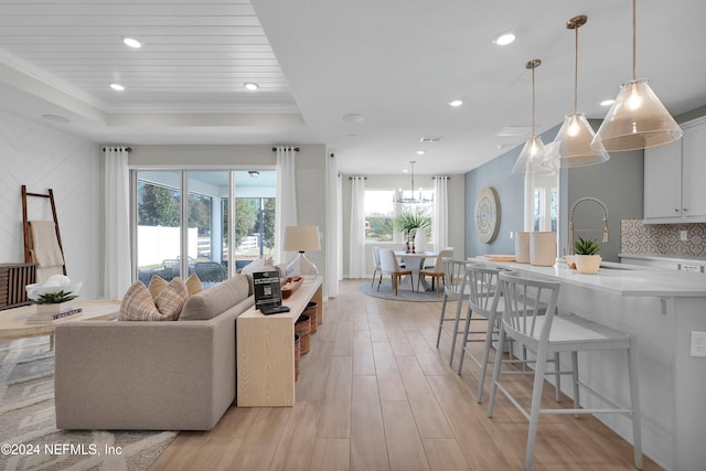 living room featuring a raised ceiling, light hardwood / wood-style flooring, crown molding, and sink