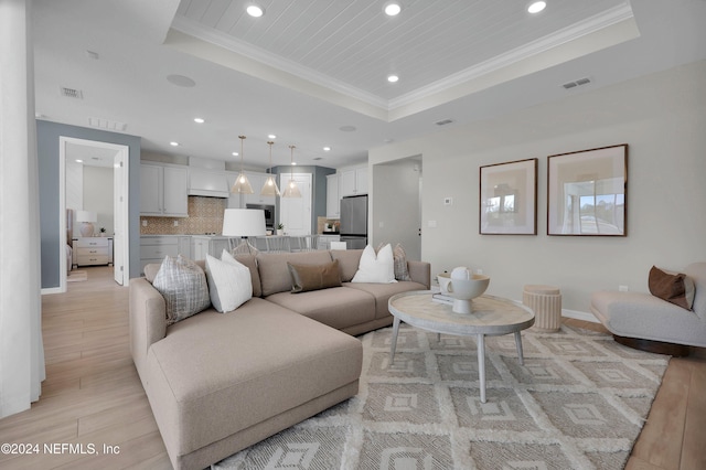 living room with a tray ceiling, crown molding, and light hardwood / wood-style floors