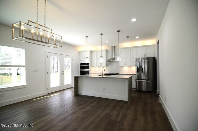 kitchen with an island with sink, white cabinets, stainless steel fridge, and wall chimney range hood