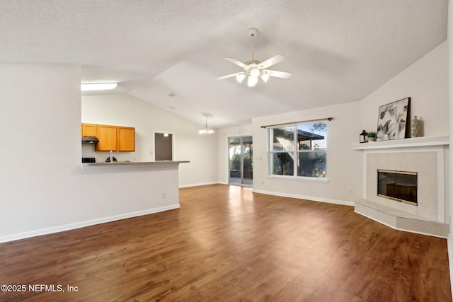 unfurnished living room featuring lofted ceiling, ceiling fan with notable chandelier, dark wood-type flooring, and a tiled fireplace