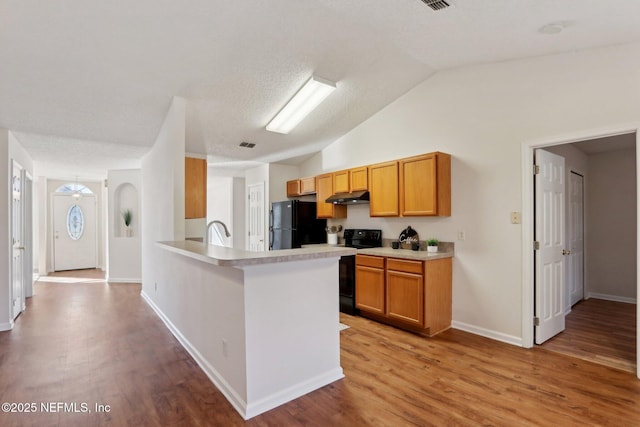 kitchen with black appliances, vaulted ceiling, a textured ceiling, light hardwood / wood-style floors, and kitchen peninsula