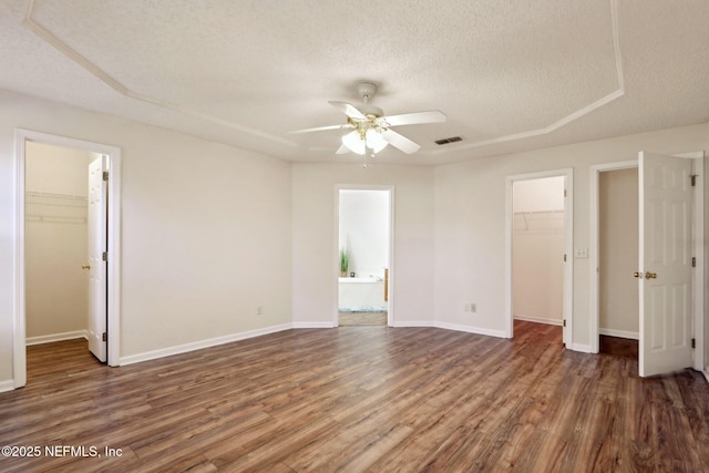 unfurnished bedroom featuring ceiling fan, dark hardwood / wood-style flooring, a spacious closet, and a textured ceiling